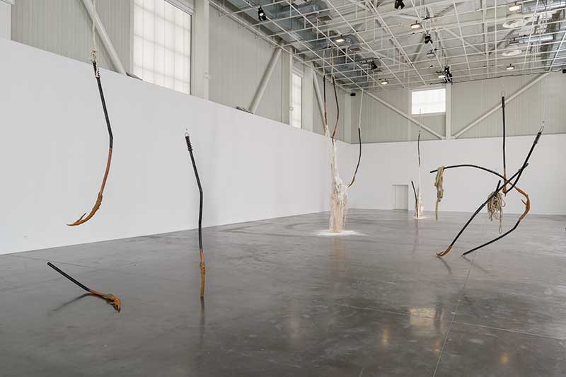 a large gallery space with an installation of sculptures that look like thin poles and sticks