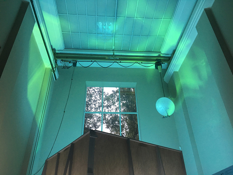a tall room with a phthalo green lit ceiling with a balloon-like object on the right