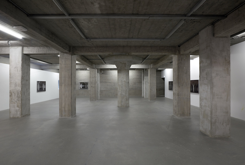 large room with concrete pillars and photographs of the room on the walls