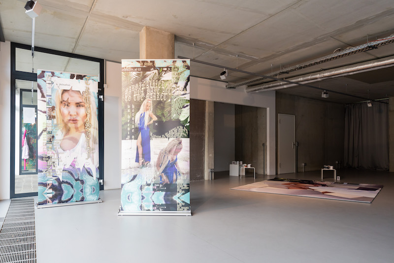 exhibition space with two colourful standing banners and a rug printed with kim kardashain 