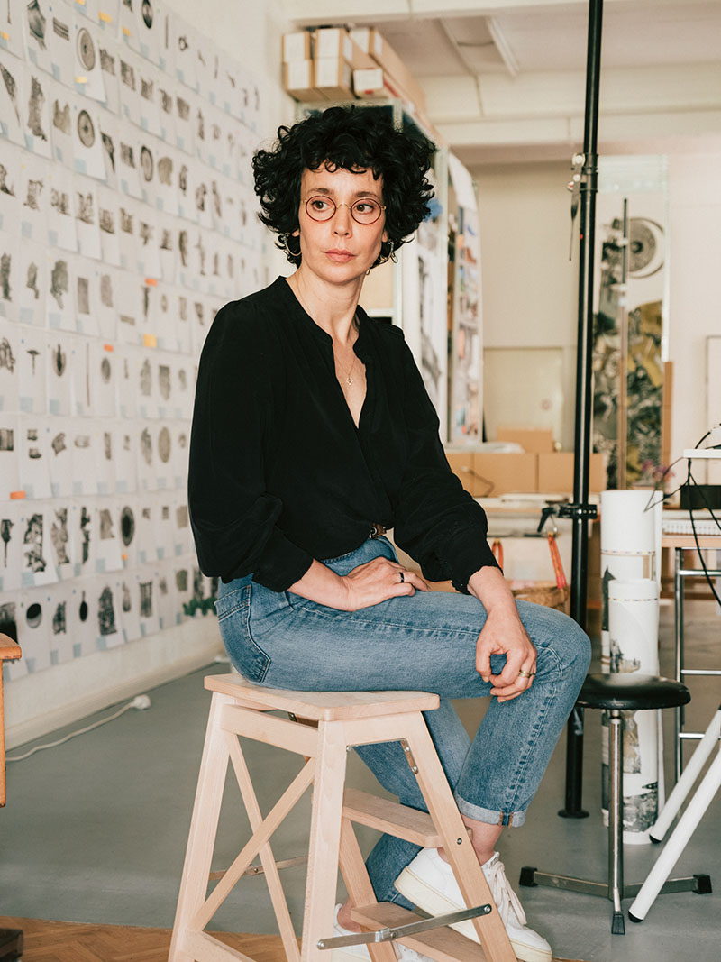 Artist Ilit Azoulay sitting on a small step ladder in her studio