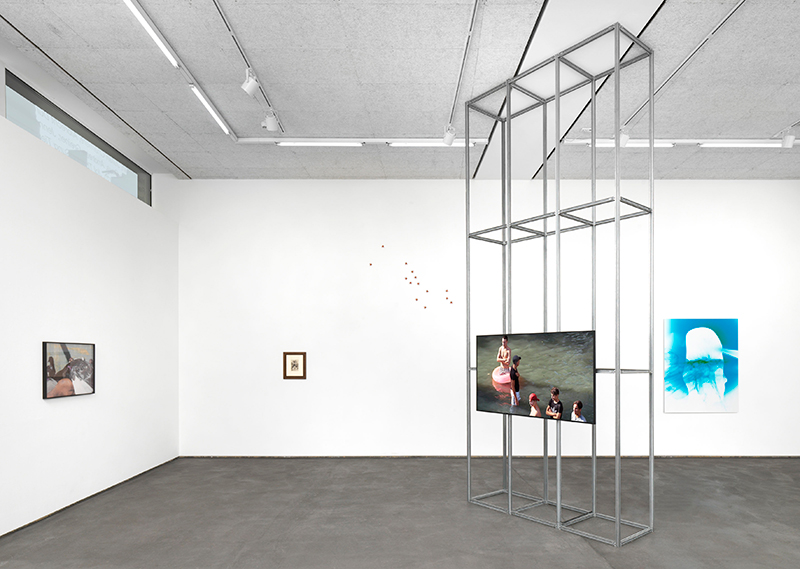a gallery space with paintings, photographs and a monitor attached to a metal structure