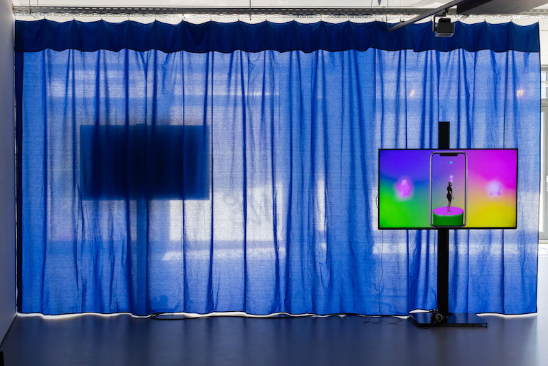 freestanding tv screen with rainbow colour background standing in front of a blue curtain