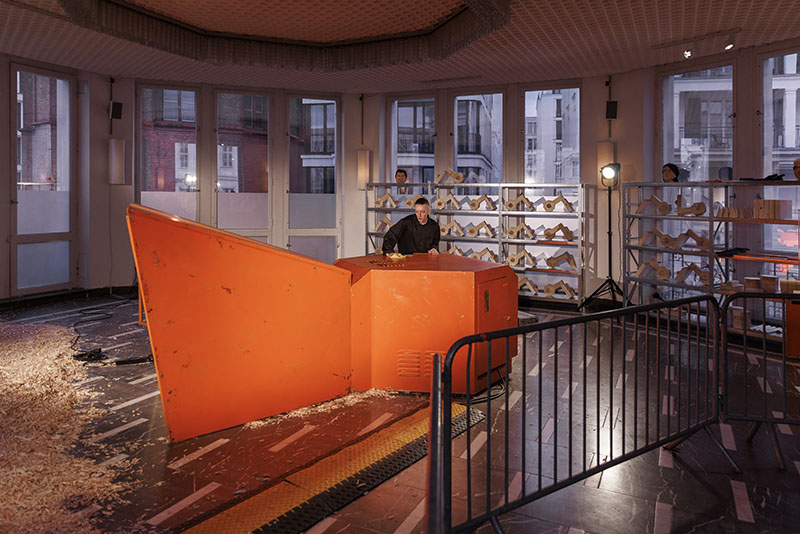 A man stands at a giant orange woodchipper as part of Pope.L's exhibition at Schinkel Pavillon