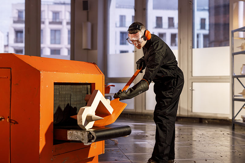 A man shreds wooden models in a giant orange woodchipper