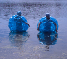 two people in blue inflatable zorbs, standing in shallow water