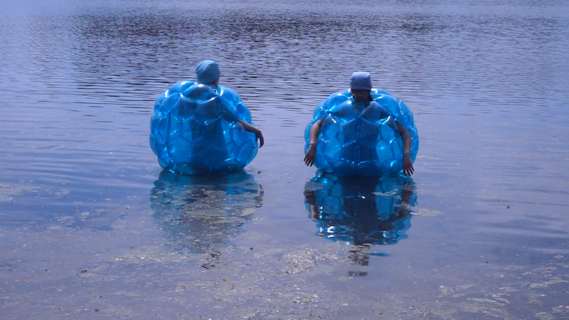 two people in blue inflatable zorbs, standing in shallow water