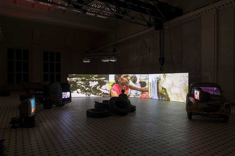 A video installation of three large projections and people sitting in front of them