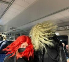 Two women wearing wigs swinging their heads around in a train
