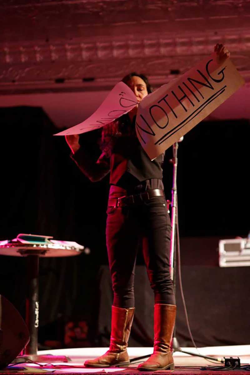 a photo of a woman on a stage ripping up a large piece of paper on which the word "nothing" is written