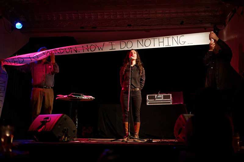 a photo of a woman on a stage with two people holding up a scroll with text above her