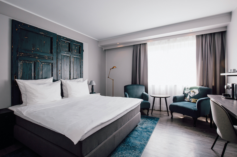 hotel suite with bed, blue carpet, blue wooden wall decoration, two blue side chairs and table