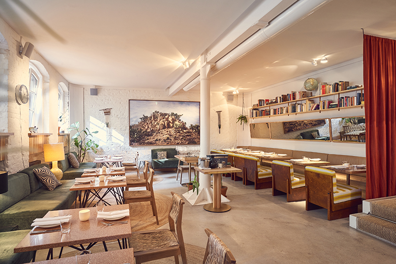 interior restaurant Panama with tables, chairs, green upholstered benches, book shelfs and a large photograph of a desert landscape on the wall