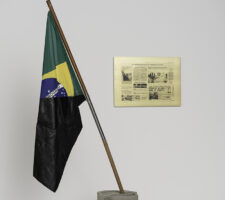 Image of a half black Brazilian flag and a framed newspaper clipping to the right of the flag