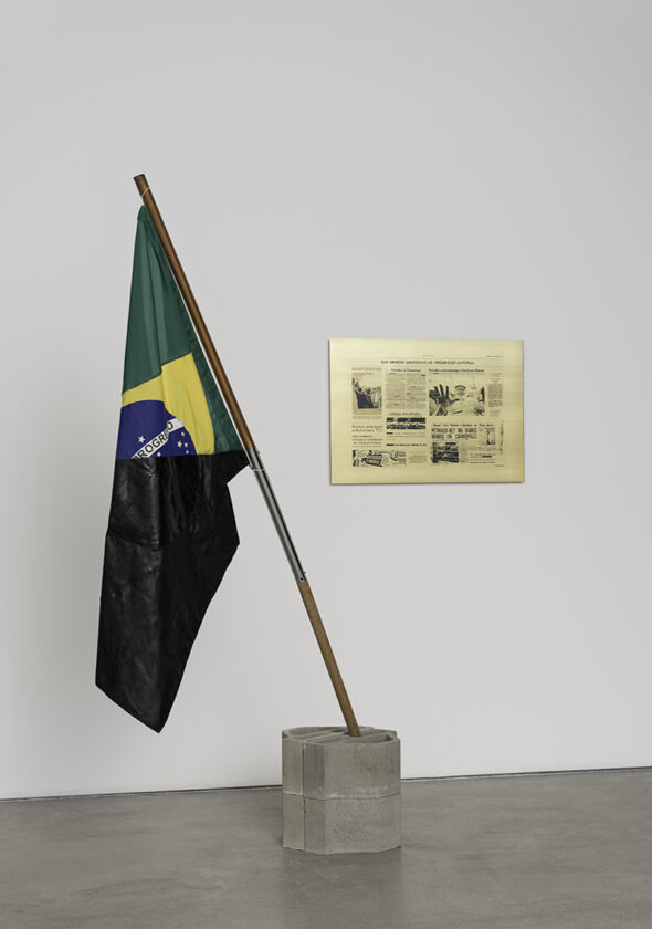 Image of a half black Brazilian flag and a framed newspaper clipping to the right of the flag 