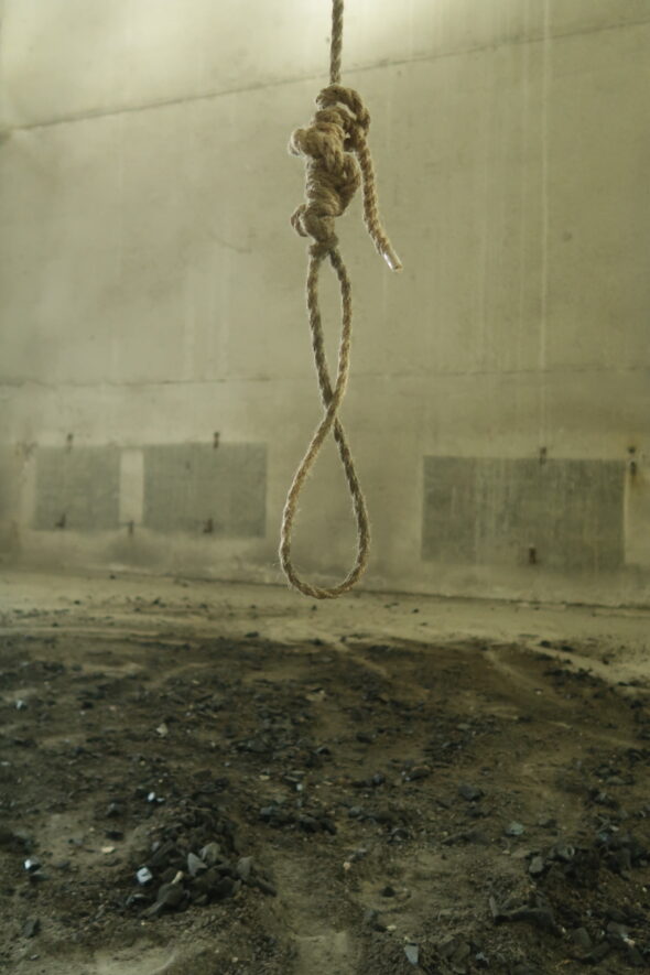 Tied rope hanging from ceiling in empty room with dirt on the floor