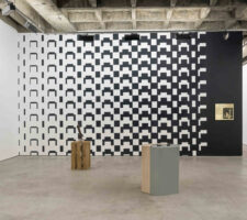 an installation view of a gallery exhibition in which a wall with a black and white pattern is scene and two plinths