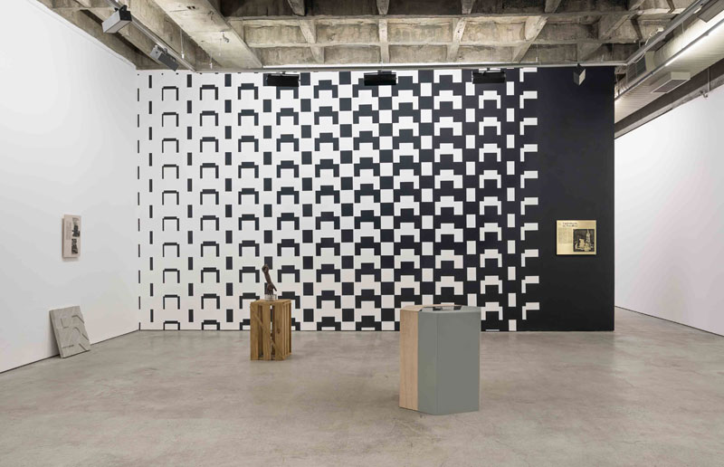 an installation view of a gallery exhibition in which a wall with a black and white pattern is scene and two plinths