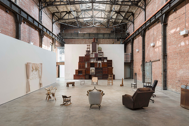 an installation of found wooden furniture piled into a sculptural form in a large warehouse-turned-museum