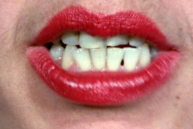 close up of a woman's lips painted in red lipstick with mouth open and crooked teeth showing