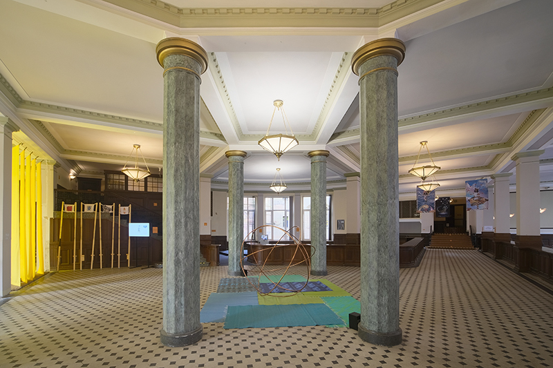 A majestic entrance lobby of an old bank with two statey columns, tiled floors and coffered ceilings