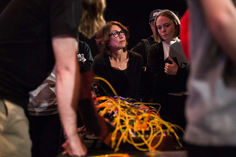 A woman photographed from behind people who are all standing together with a number of cables visible in the foreground