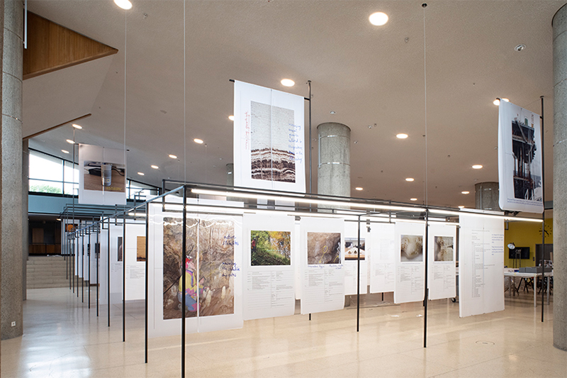 Large prints on paper hanging on metal scaffolding in the foyer of a museum