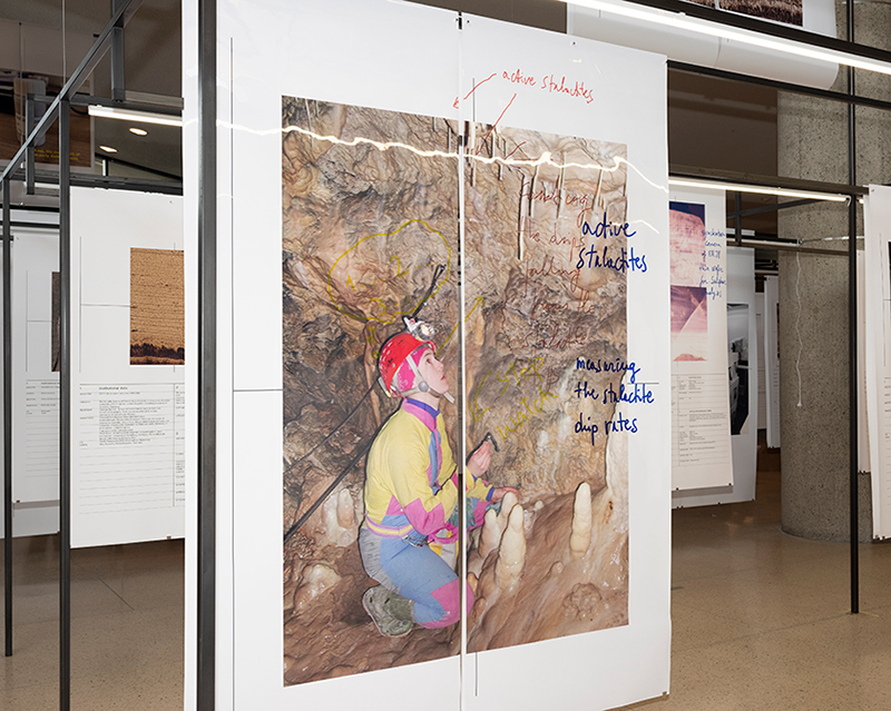 A large print of a scientist in a cave with written text on top hanging on metal scaffolding