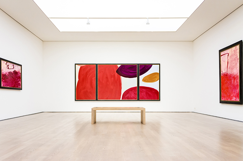 A gallery with three large abstract paintings on the walls and a bench in the middle
