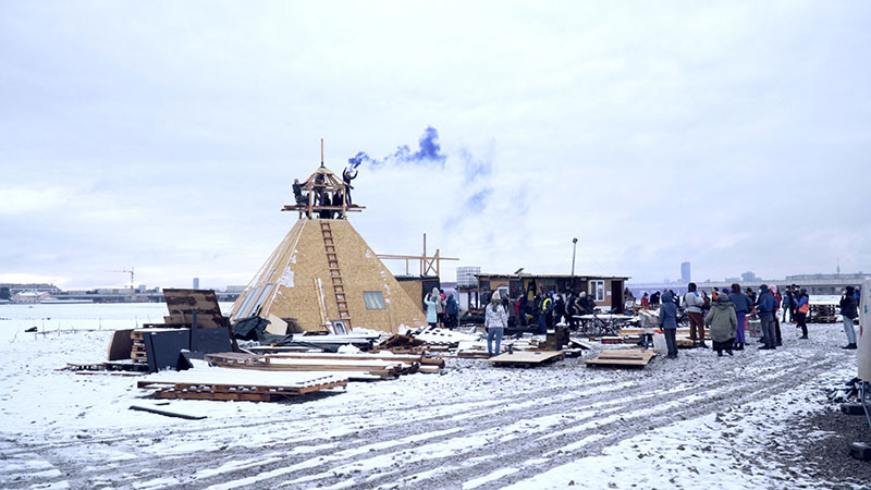 a snowy scene in which a teepee-like structure made out of wood stands as part of a protest