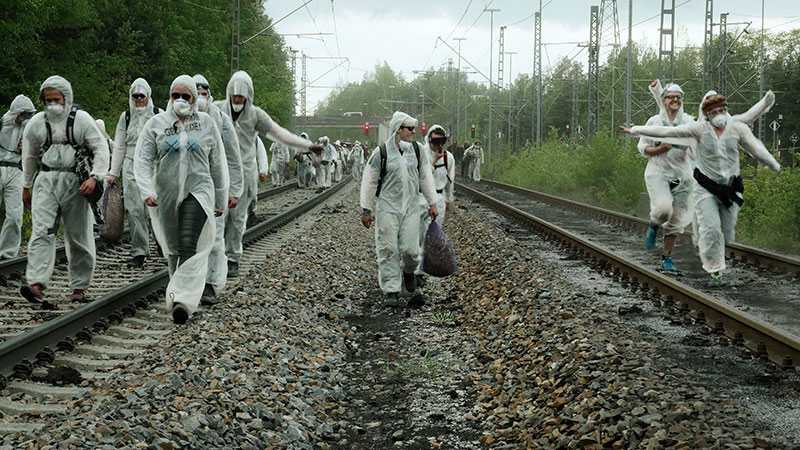 People in white hazmat walking on train tracks in a forested area