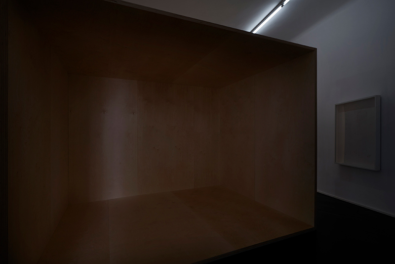 a dimly lit gallery space with a large hollow wooden box structure in it