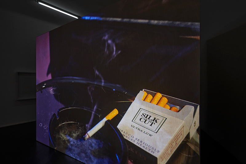 A projection of a CGI animation of a smoking cigarette in an ashtray and a pack of open cigarettes