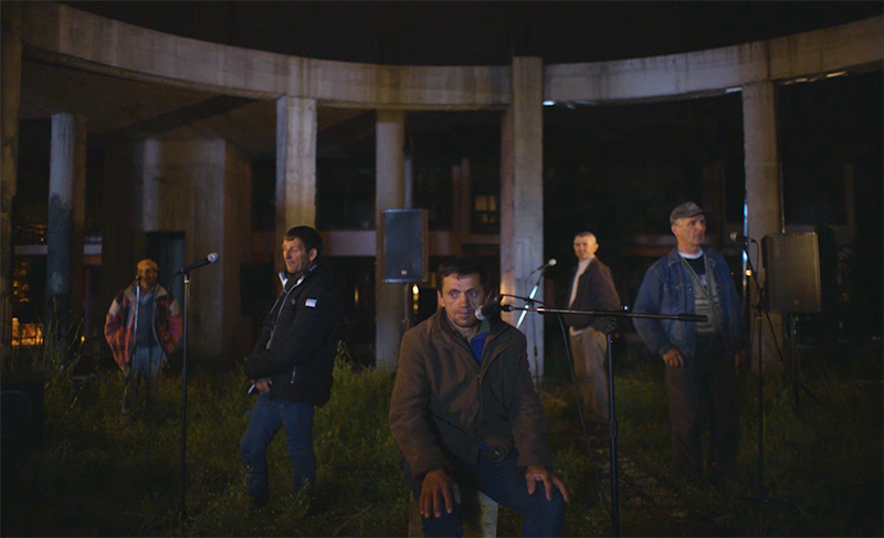 men standing in front of microphones at night in ruins