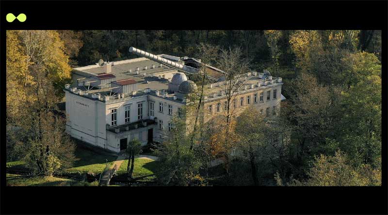 Birds eye photo of the Archenhold Observatory, a white, classical building with a big telescope set in a forested area