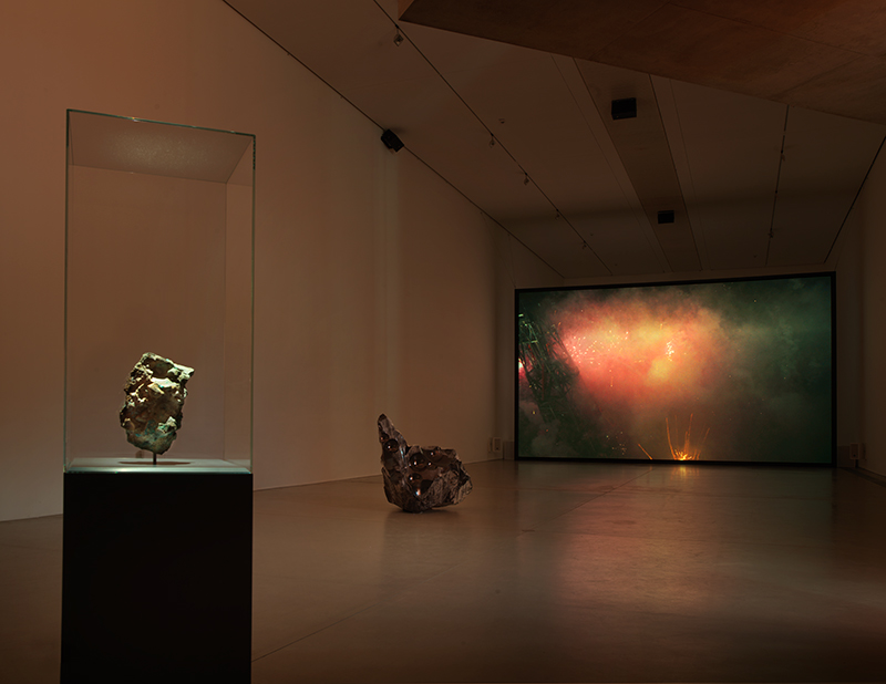 a dimly lit gallery space with a video projection and sculpture
