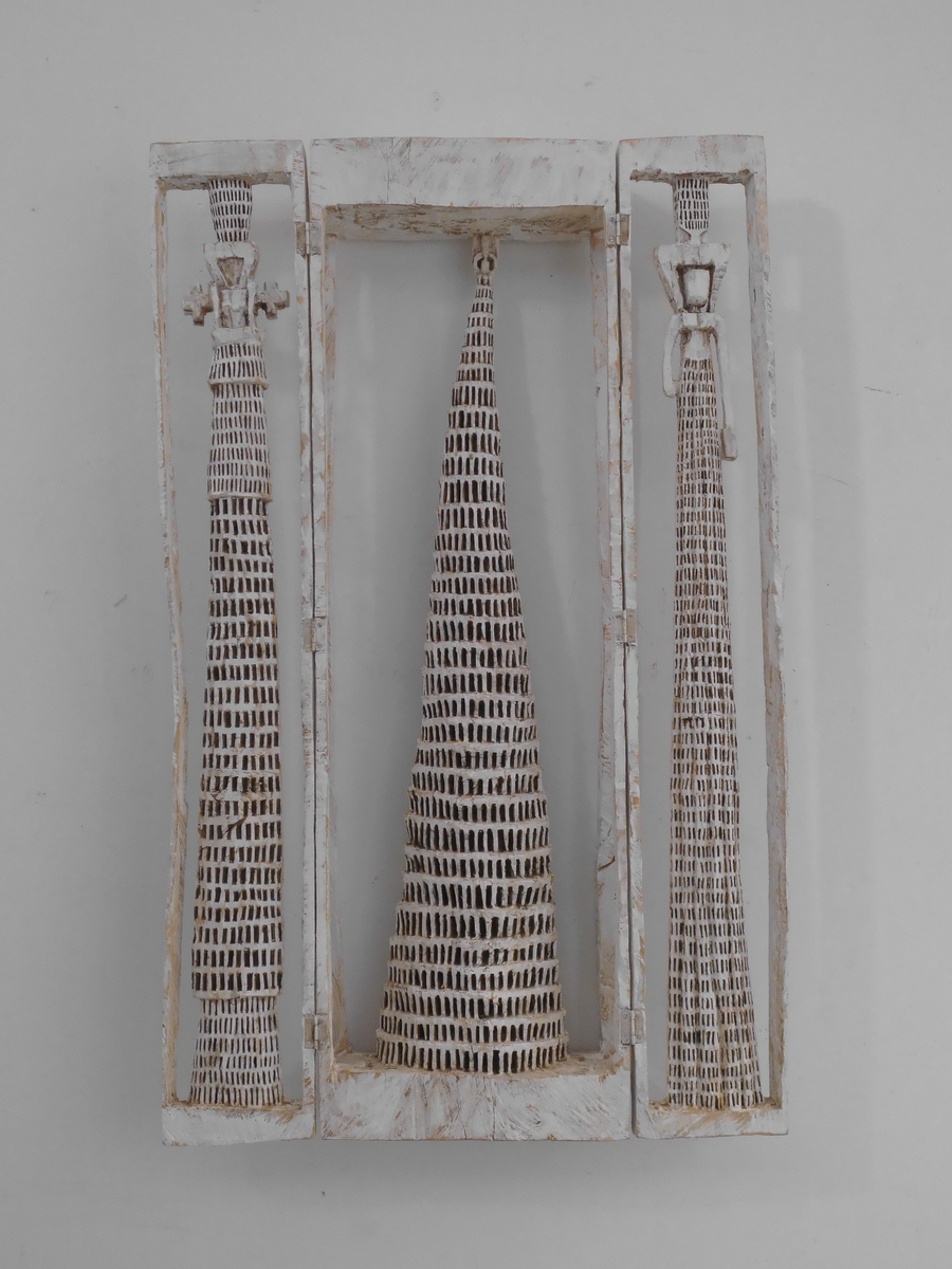 a wood-cut sculpture that hangs on the wall consisting of three towers with honeycombed texture