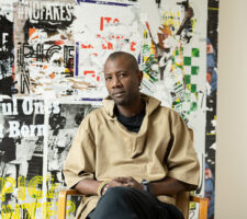 portrait of a black Angolan artist sitting in front of his collages