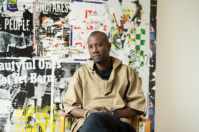 portrait of black Angolan artist Yonamine sitting in front of his collages