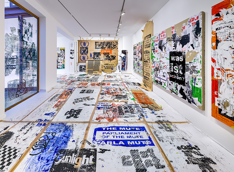 A gallery installation view of posters taken off the streets and plastered on the walls and floor