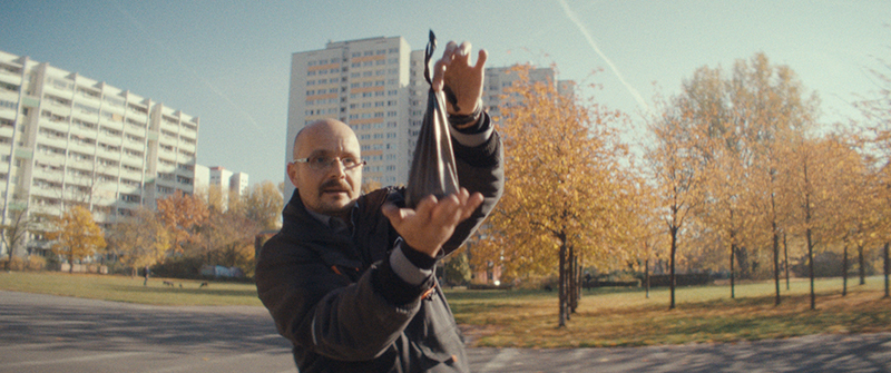 A man holds up a small bag filled with dog poop in a neighbourhood of high rise apartment buildings