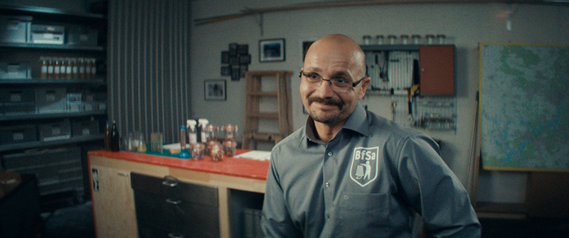 film still featuring a man smiling in what looks like a workshop