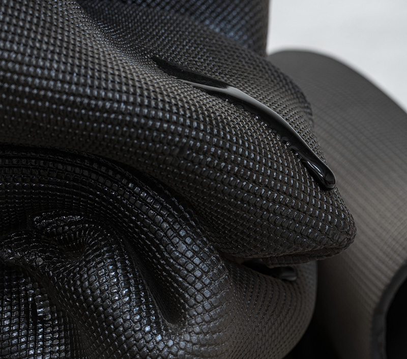 A black substance that looks like rippled cloth folding on itself but is actually ceramic with a liquid trickling over its side