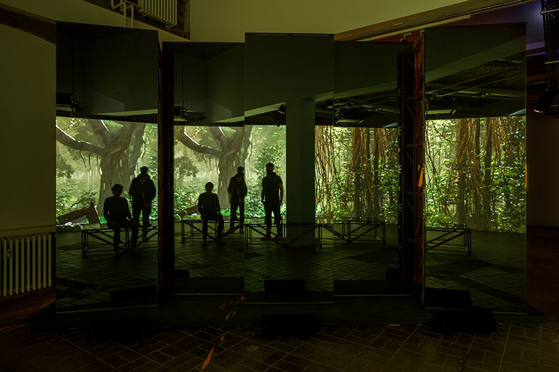 A photo of silhouettes of people standing in front of a wide screen projection of a jungle