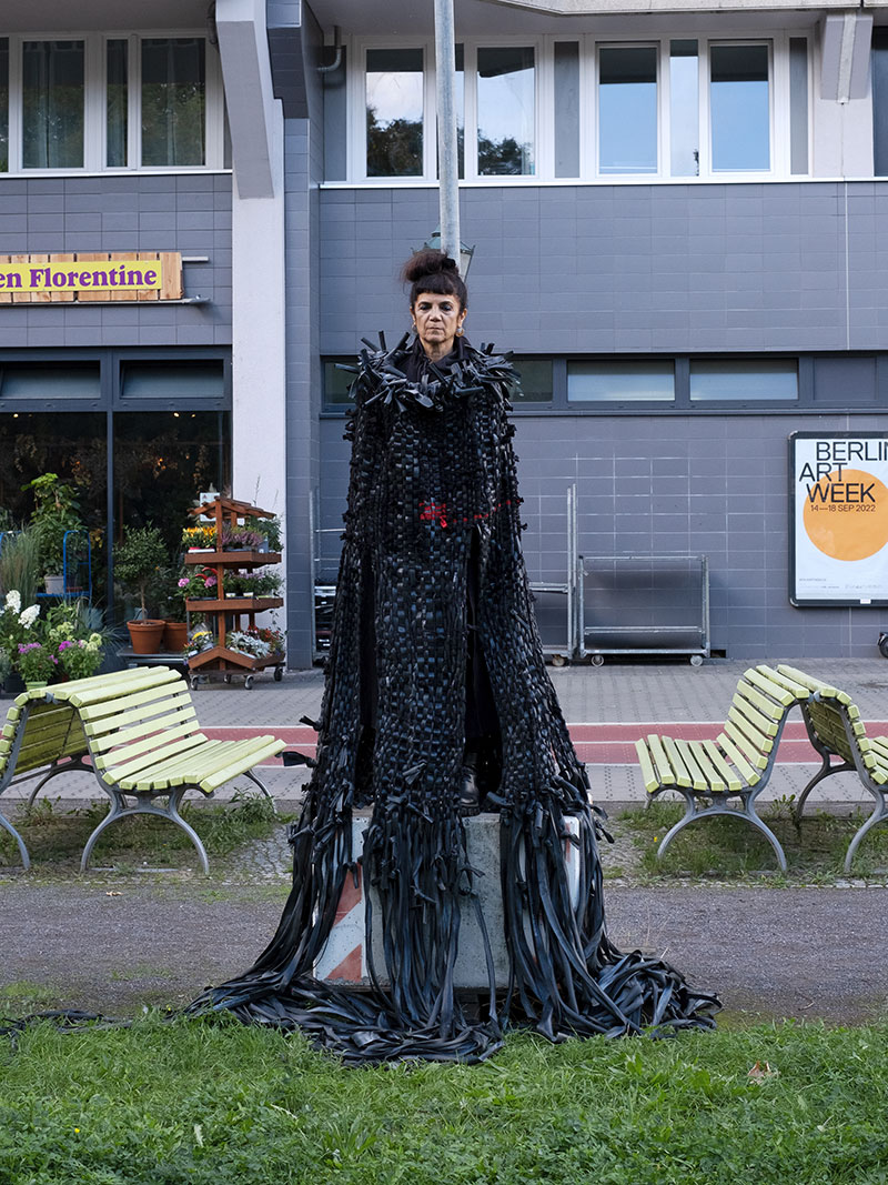 A woman standing on a pedestal in a public place wearing a very long black robe-like dress