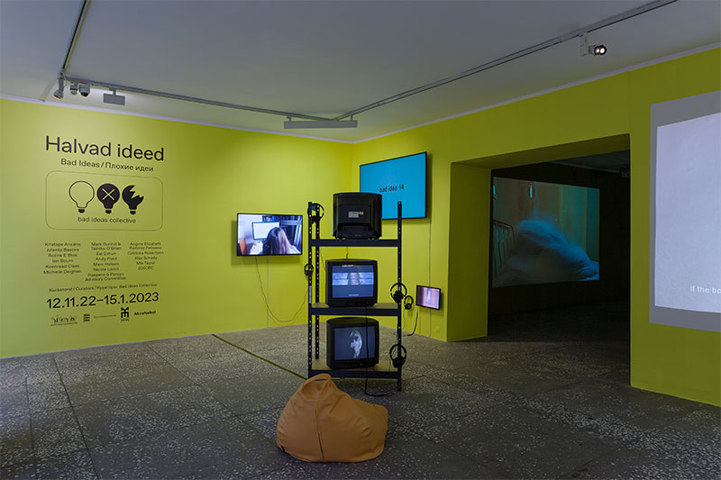 a photo of a gallery installation wherein the gallery is painted yellow and monitors of different shapes and sizes are installed