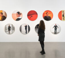 person looking at nine circle-shaped photographs on a wall in an exhibition space