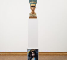 Nefertiti bust wearing sunglasses standing on a pedestal against which leans a photograph showing Mona Lisa