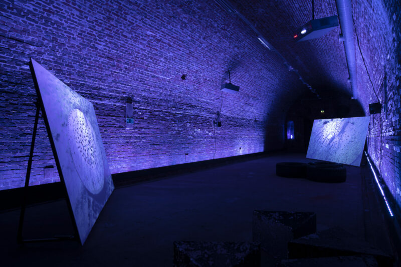 two screens placed in a gunpowder cellar illuminated with purple light