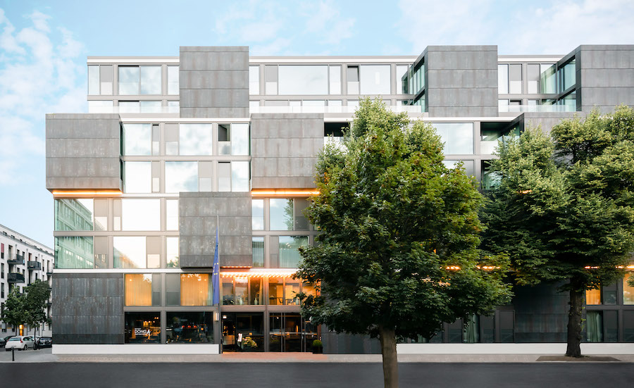 Exterior View of the concrete and glas facade of hotel KPM in Berlin with two green trees in the forefront